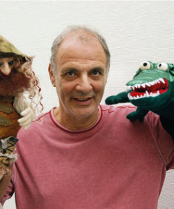 Horst Basting agiert mit zwei Handpuppen. Es handelt sich um eine Puppe mit langem Haar, Vollbart und Hut und um ein grünes Krokodil mit offenem Maul.