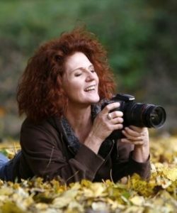 Foto von Christine Steimer auf dem Bauch im Laub liegend, mit der Kamera im Anschlag.